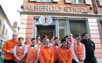 Immagine dei dipendenti dell'Albergo Etico di Asti, ragazzi con la Sindrome di Down, con indosso divisa arancione della struttura ricettiva, mentre posano davanti all'insegna dell'albergo