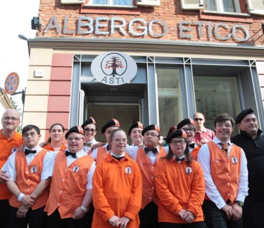 Immagine dei dipendenti dell'Albergo Etico di Asti, ragazzi con la Sindrome di Down, con indosso divisa arancione della struttura ricettiva, mentre posano davanti all'insegna dell'albergo