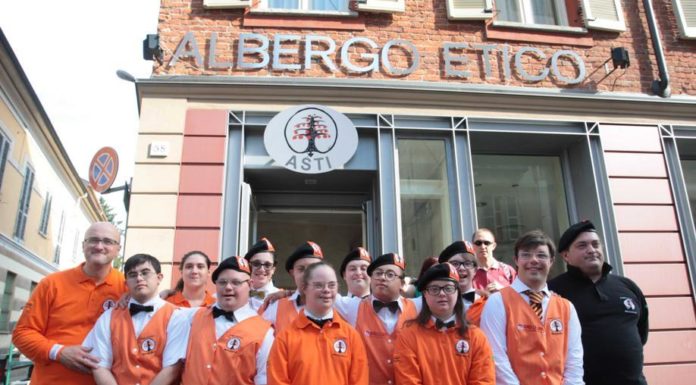 Immagine dei dipendenti dell'Albergo Etico di Asti, ragazzi con la Sindrome di Down, con indosso divisa arancione della struttura ricettiva, mentre posano davanti all'insegna dell'albergo