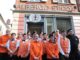 Immagine dei dipendenti dell'Albergo Etico di Asti, ragazzi con la Sindrome di Down, con indosso divisa arancione della struttura ricettiva, mentre posano davanti all'insegna dell'albergo